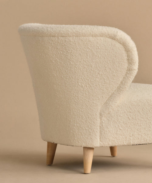 The Brentwood Chair features a modern curved backrest, ivory wool boucle upholstery, and light wooden legs, shown against a beige background.