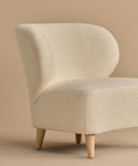 The Brentwood Chair features a curved backrest and soft ivory Belgian Wool Boucle upholstery, supported by four light wood legs, all showcased against a beige background.