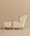 A cream-colored wool boucle upholstered armchair with wooden legs is paired with the matching Brentwood Ottoman, both set against a plain beige background.