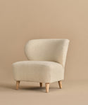 The Brentwood Chair features a modern armless design with a curved backrest, light wooden legs, and cream Belgian Wool Boucle upholstery, shown against a plain beige background.