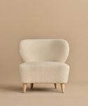 The Brentwood Chair is a modern piece, upholstered in ivory wool boucle with cream tones and light wood legs, shown against a plain beige background.