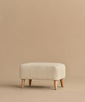 The Brentwood Ottoman features a minimalist design in light beige wool boucle with short wooden legs, showcased against a solid beige background.