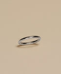The Brook Gold Band, a slim white gold ring, rests on a plain beige surface with a subtle shadow beneath.