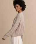 Woman with curly hair wearing the Cable Serena Crewneck sweater and an off-white skirt, standing sideways against a plain beige background.