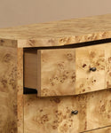A close-up of the Carbon Dresser shows its unique, swirled burlwood pattern. One soft-close drawer is partially open, revealing a simple wood interior. Each drawer is accented with small, round black knobs.