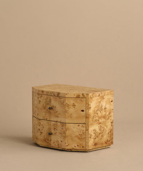 The Carbon Nightstand is a small, modern piece with two drawers, round metal knobs, and a light burled wood finish featuring a natural textured pattern, shown against a plain beige background.