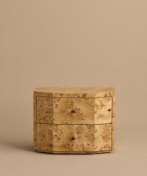 The Carbon Nightstand is a compact, lightweight piece featuring a natural burled wood grain, two drawers with round metal knobs, and a modern design, displayed against a plain beige background.