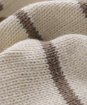 A close-up of a knitted cream fabric with thick ivory taupe stripes highlights the Chloe Cardigan’s textured yarn and stylish pattern—ideal for lightweight, warm-weather sweaters.