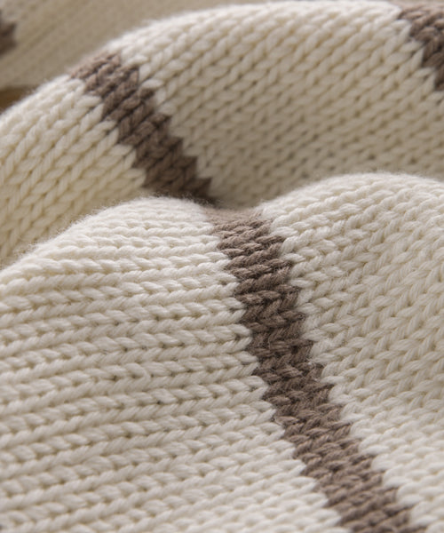 A close-up of a knitted cream fabric with thick ivory taupe stripes highlights the Chloe Cardigan’s textured yarn and stylish pattern—ideal for lightweight, warm-weather sweaters.