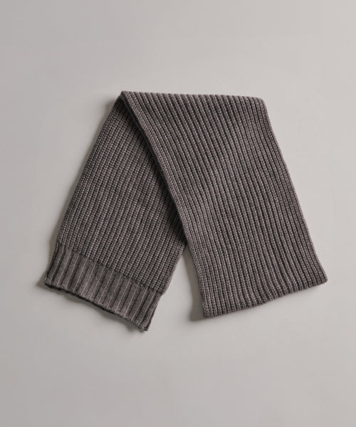 The Cashmere Alpine Scarf, featuring a chunky ribbed design in gray, is laid flat on a light gray surface.