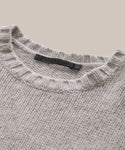 A close-up of the Cashmere Amelia Crewneck, a grey cashmere knit sweater with a ribbed crew neckline and black label inside the collar, displayed on a neutral beige background.
