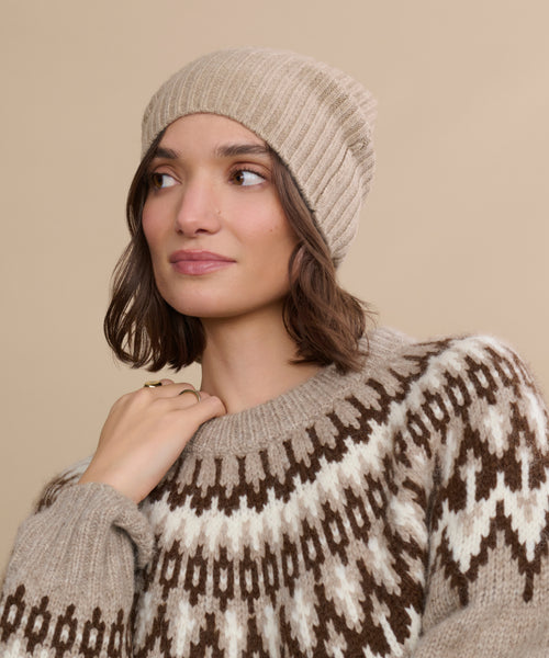 A woman wearing a Cashmere Beanie and a beige and brown patterned sweater looks to the side against a matching beige background.