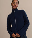 A person wears the Boyd Cashmere Sweater in navy blue with a fisherman rib zip-up design and high mock neck, standing against a plain beige background and looking at the camera with a slight smile.