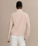 A person with their hair in a bun is shown from the back, wearing the cream Boyd Cashmere Sweater and white pants, standing against a plain beige background.