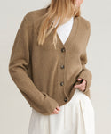 A person wears the brown Cashmere Colette Cardigan over a white top and high-waisted pleated white trousers, with their face partially out of view.