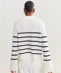 A person with dark hair in a bun is seen from the back, wearing the Cashmere Frances Polo—a relaxed fit knit with navy stripes and wide sleeves—paired with white pants against a plain light background.