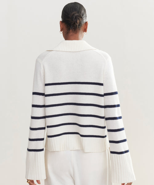 A person with dark hair in a bun is seen from the back, wearing the Cashmere Frances Polo—a relaxed fit knit with navy stripes and wide sleeves—paired with white pants against a plain light background.