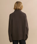 A person with blonde, chin-length hair is shown from behind wearing the Cashmere Jet Turtleneck in dark brown and dark pants against a plain beige background.