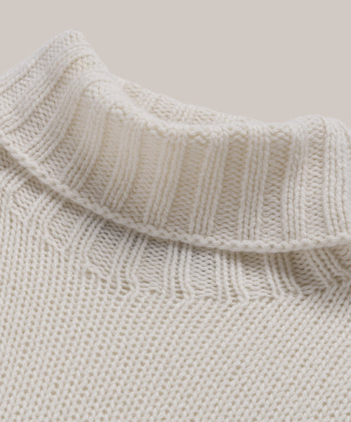 Close-up of the Cashmere Jet Turtleneck, a cream-colored ribbed oversized sweater, showcasing the lightweight knit texture and pattern against a neutral background.