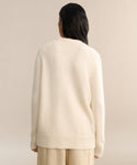 A person with long dark hair, seen from behind, wears the Cashmere Kate V-Neck in ivory and beige pants, standing against a plain light beige background.