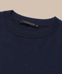 Close-up of the collar and upper section of the dark navy Cashmere Marina Crewneck sweater, featuring a visible black label, set against a neutral beige background.