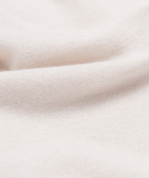 A close-up of the Cashmere Marina Crewneck in soft, light beige, featuring a subtly textured surface and gentle folds—evoking smoothness and coziness, ideal for a relaxed spring sweater silhouette.