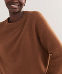 A person is smiling, wearing the Cashmere Oversized Crewneck in soft brown with a relaxed fit. Only their upper body and part of their face are visible against a plain, light background.