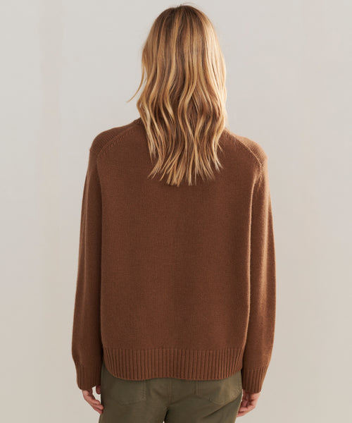 A person with long, wavy blonde hair is seen from behind, wearing the Cashmere Oversized Crewneck and olive green pants, standing against a plain light-colored background.