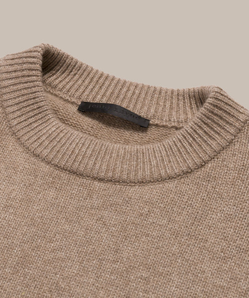 Close-up of the Cashmere Oversized Crewneck in beige, featuring a ribbed neckline and black label inside the collar, laid flat on a neutral background.