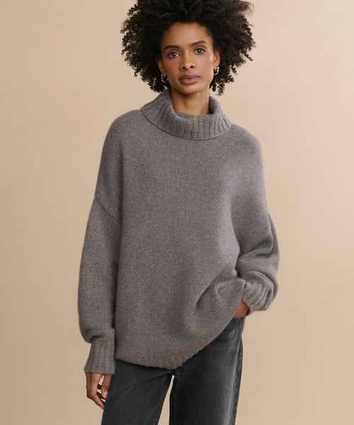 A woman poses for a photo, elegantly dressed in the Cashmere Porter Turtleneck, its oversized silhouette draping softly around her frame.