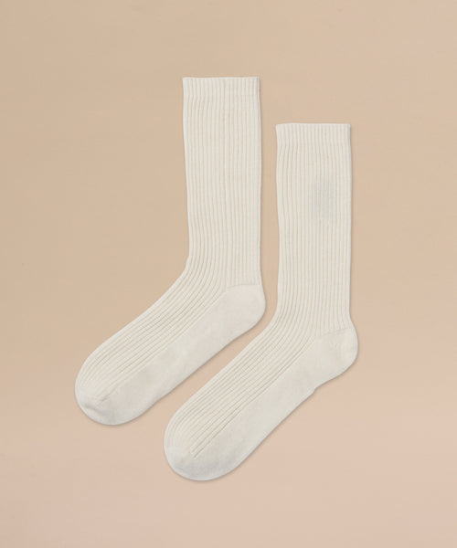 A pair of Cashmere Socks in ivory with a ribbed crew design, perfect for fall and winter, laid flat on a beige background with toes pointing to the lower left corner.