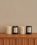 Four hand-poured Cedar Glass Candles in black and white containers sit on a wooden surface against a beige wall, each labeled with a scent—Cedar, Aspen, Topanga, and Musk—perfect for gifting and worthy of Oprah’s Favorite Things.