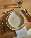 A dining table set with a Pacific Salad Plate, brown-handled cutlery, a folded white napkin, and a glass of water, all arranged on a light wooden surface.