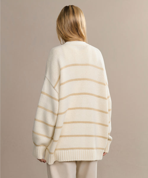 A person with long blonde hair is seen from behind, wearing the Chloe Cardigan and beige pants, standing against a plain beige background—a stylish pick for your spring and summer wardrobe.