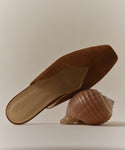 A Clara Mule—an Italian-made shoe with jenn kayne on the insole—rests atop a large seashell against a neutral background.