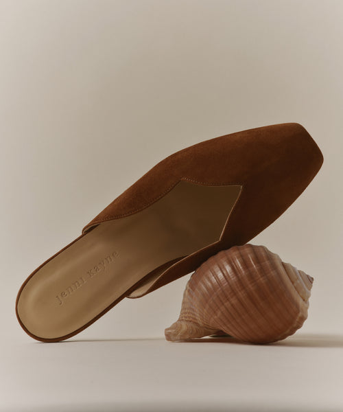 A Clara Mule—an Italian-made shoe with jenn kayne on the insole—rests atop a large seashell against a neutral background.