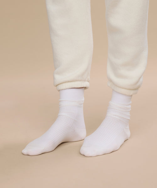 A person wearing Classic Sock and cream-colored, rolled-up pants stands on a beige background, with focus on their lower legs and feet.