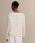 A person with hair in a neat bun wears the Claude Long-Sleeve Tee, featuring nautical stripes, and loose white pants while standing against a plain beige background, shown from the back.