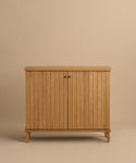 The Coast Hutch is a solid white oak cabinet with vertical slats, two central doors, small black handles, and short angled legs in a mid-century modern hutch design, shown against a beige background.
