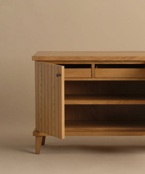 The Coast Sideboard is a Mid-Century Modern wooden sideboard with angled legs, two small drawers, and an open cabinet door showing two interior shelves, all displayed against a plain beige background.