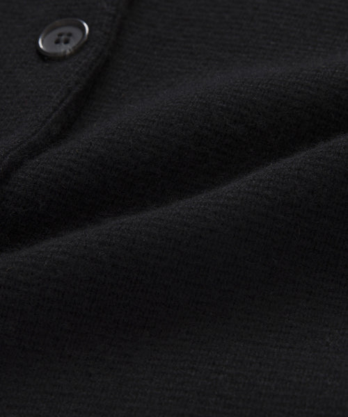 Close-up of the textured black fabric on the Cooper Cardigan, with a visible seam and part of a black button. The soft, slightly folded material highlights the quality finish of this structured cardigan.