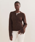 A woman wears the Cooper Cardigan, a dark brown button-up with a structured silhouette, over a white top and pants against a light background, illustrating its versatile styling for any occasion.