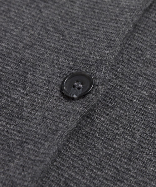Close-up of a black button sewn onto textured, dark grey knit fabric from the Cooper Cardigan. Buttonhole and stitch details are visible.