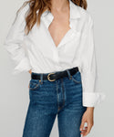 Someone wears the Boyfriend Shirt in white, partially unbuttoned and tucked into high-waisted blue jeans with a black belt. Their hair is loose as they stand against a plain background.