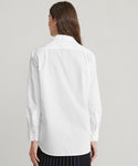 A woman with long brown hair is seen from behind wearing the Boyfriend Shirt—an oversized, long-sleeve white shirt—against a simple light background, capturing a laid-back and timeless look.