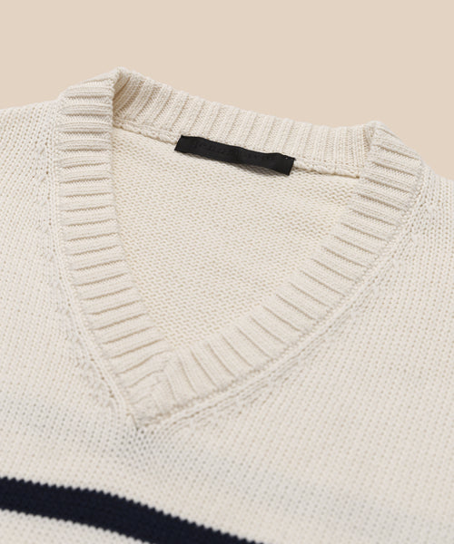 Close-up of the Cotton Kate V-Neck, a cream-colored striped sweater with a ribbed cotton V-neck collar and black label inside the neckline. A dark horizontal stripe adds to its classic spring knit style.