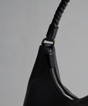 Close-up of the Crescent Shoulder Bag, crafted from soft leather in Italy, with a silver zipper and braided handle, shown against a plain light gray background.