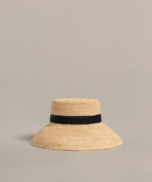 The Crochet Raffia Sun Hat features a wide brim and a black band around the crown, displayed against a plain, neutral background.