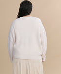 A person with long dark hair is shown from the back, wearing the Cropped Cashmere Cocoon Cardigan and a light pleated skirt against a beige background.