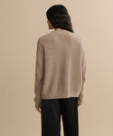 A person with long, dark wavy hair is seen from behind in the Cropped Cashmere Cocoon Cardigan and black pants, standing against a plain beige background.